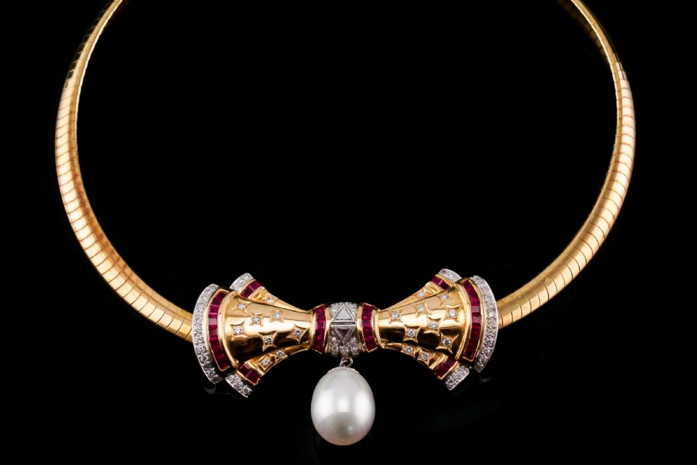 A structured 18k yellow gold collar necklace featuring a central bow motif accented with rubies and star-set diamonds above a teardrop pearl. View XV
