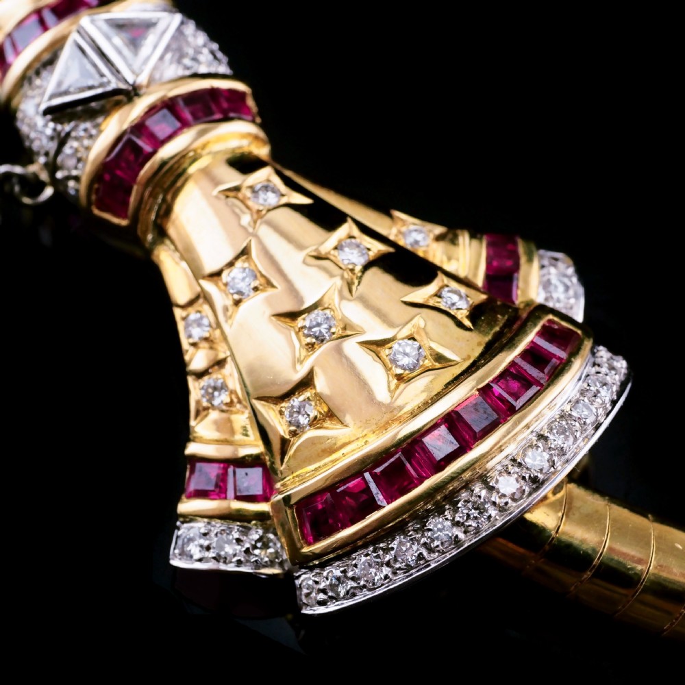 A structured 18k yellow gold collar necklace featuring a central bow motif accented with rubies and star-set diamonds above a teardrop pearl. View XXI