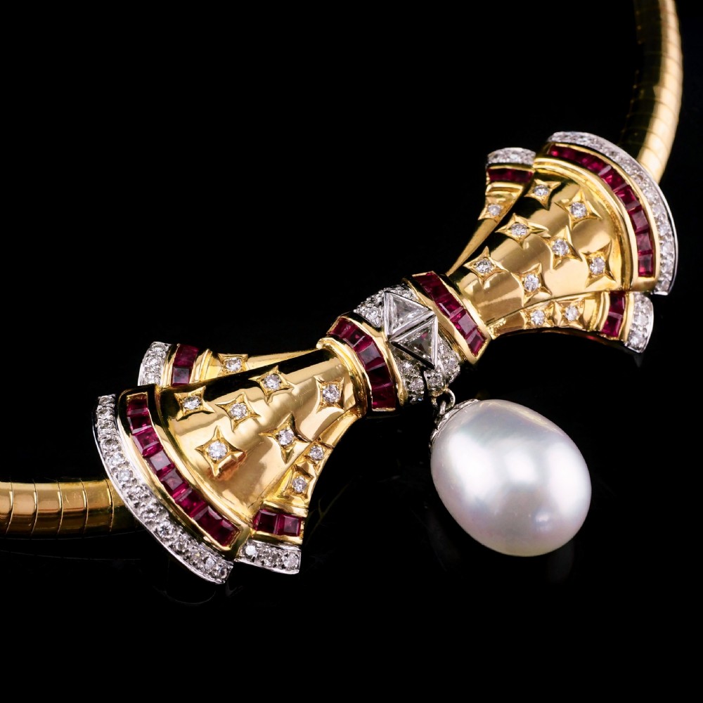 A structured 18k yellow gold collar necklace featuring a central bow motif accented with rubies and star-set diamonds above a teardrop pearl. View XXIV