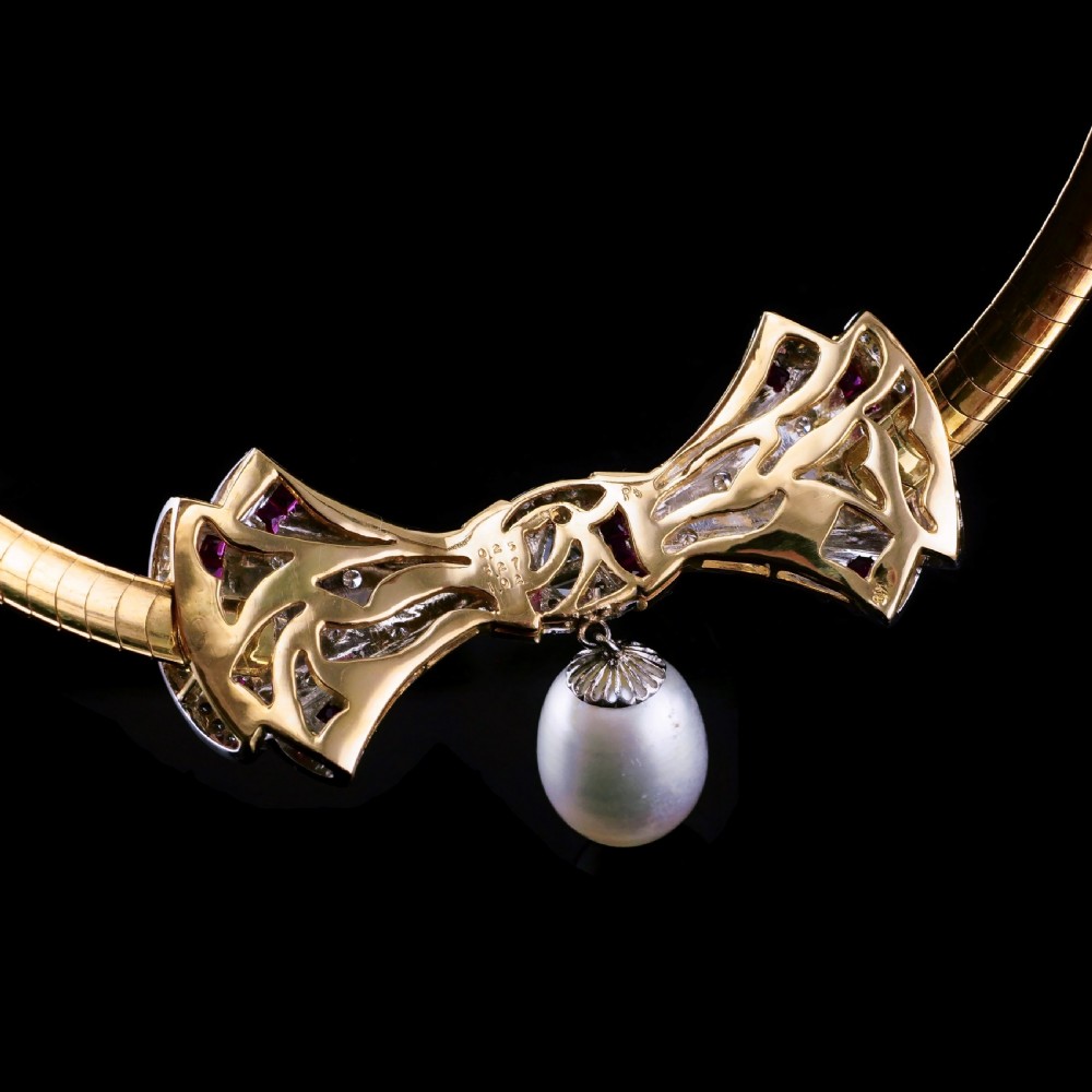 A structured 18k yellow gold collar necklace featuring a central bow motif accented with rubies and star-set diamonds above a teardrop pearl. View XXV