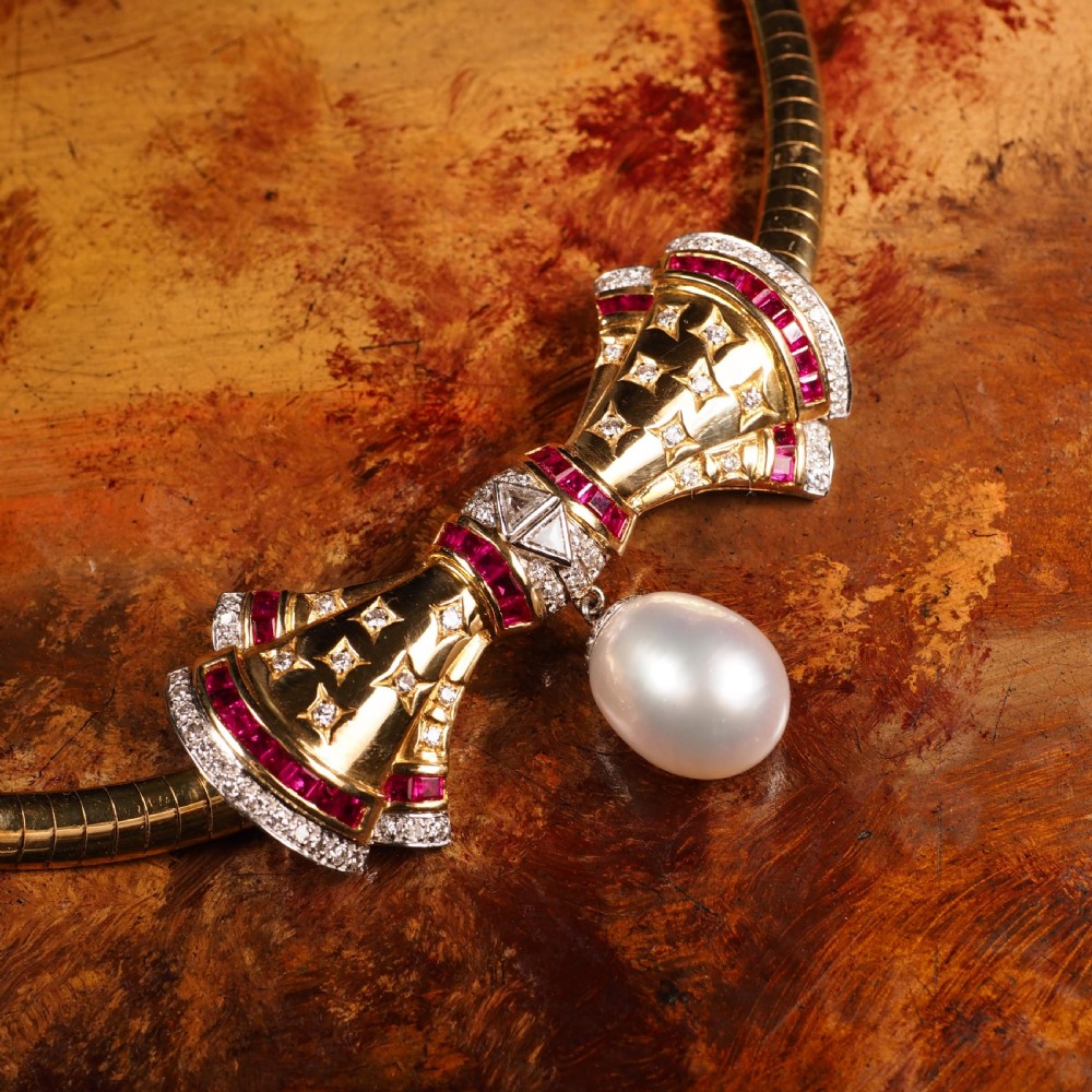 A structured 18k yellow gold collar necklace featuring a central bow motif accented with rubies and star-set diamonds above a teardrop pearl. View XXX