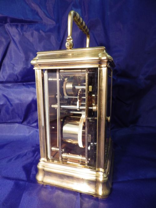 fig 1. A rectangular brass repeating carriage clock featuring a top carrying handle, glass side panels, an engraved brass mask, and a white enamel dial with Roman numerals.