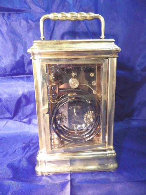 fig 2. A rectangular brass repeating carriage clock featuring a top carrying handle, glass side panels, an engraved brass mask, and a white enamel dial with Roman numerals.