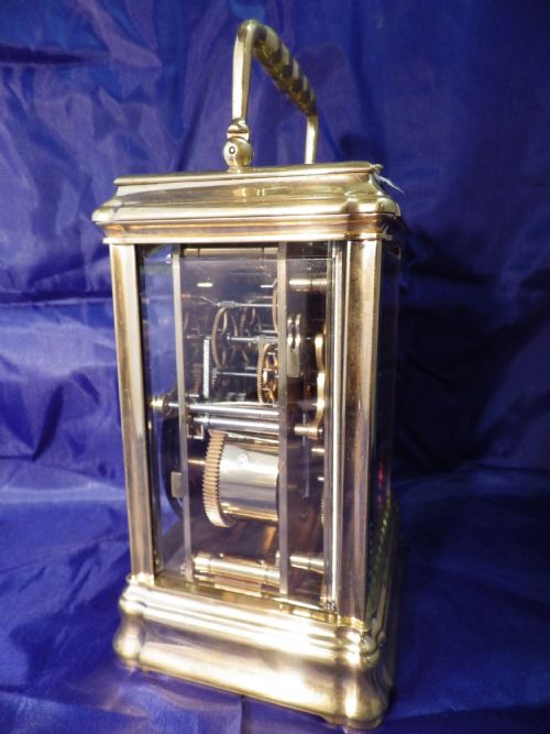fig 3. A rectangular brass repeating carriage clock featuring a top carrying handle, glass side panels, an engraved brass mask, and a white enamel dial with Roman numerals.