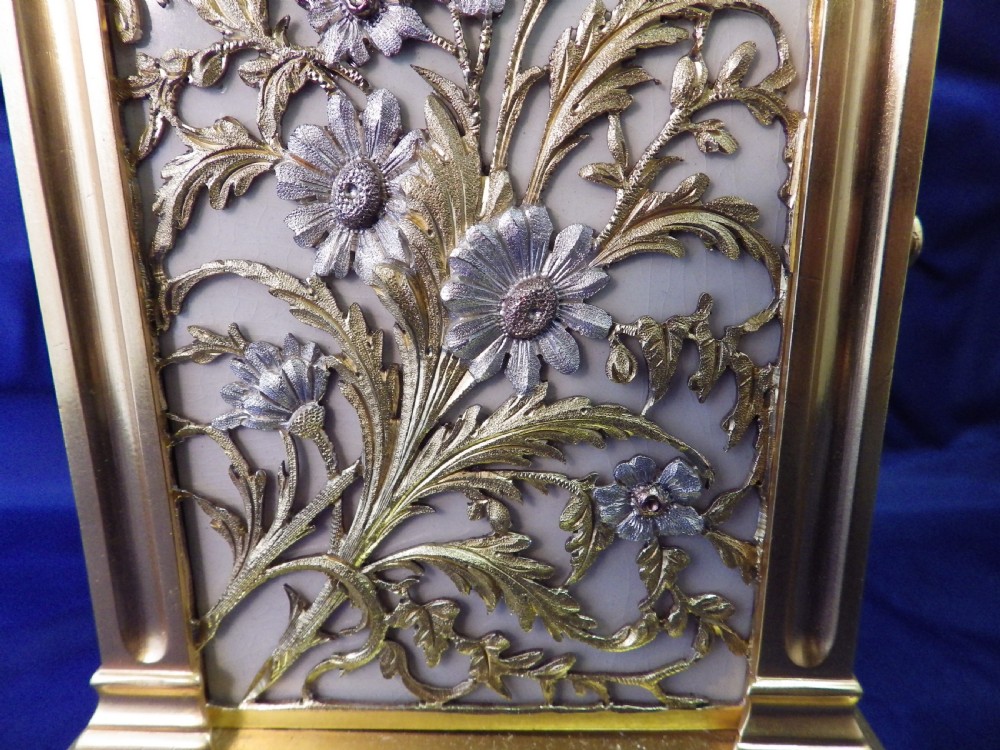 A gilt brass French repeating carriage clock featuring fluted corner columns, an intricate floral dial plate with enamel numerals, and a top carrying handle. View VI