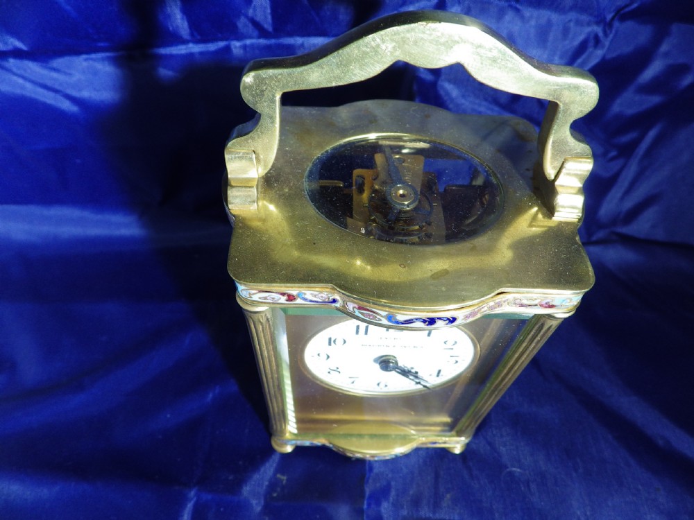 A rectangular gilded brass carriage clock featuring champleve enamel borders, glass panels, and a white dial with Arabic numerals. View V