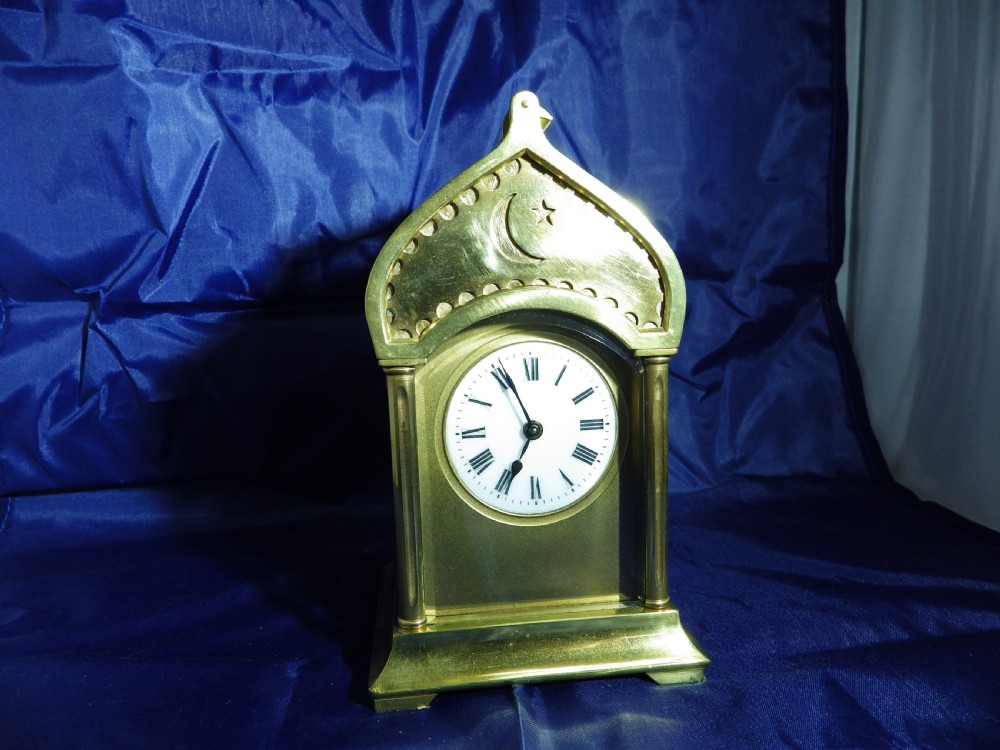 A brass French carriage clock featuring an arched canopy with an engraved crescent moon and star motif above a white enamel dial with Roman numerals. View II