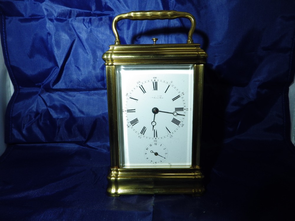 A rectangular gilt brass carriage clock with bevelled glass panels, a top carrying handle, and a white enamel dial with Roman numerals. View II