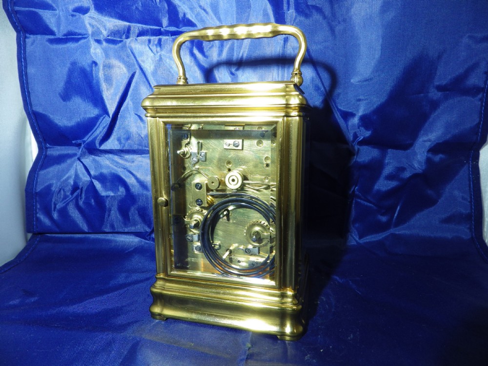 A rectangular gilt brass carriage clock with bevelled glass panels, a top carrying handle, and a white enamel dial with Roman numerals. View III