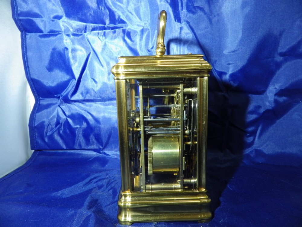 A rectangular gilt brass carriage clock with bevelled glass panels, a top carrying handle, and a white enamel dial with Roman numerals. View IV