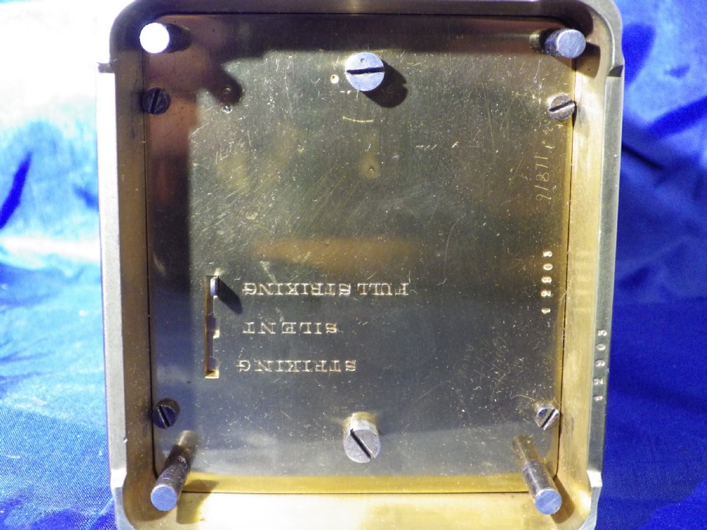 A rectangular gilt brass carriage clock with bevelled glass panels, a top carrying handle, and a white enamel dial with Roman numerals. View V