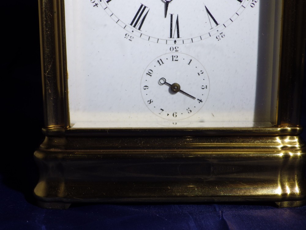 A rectangular gilt brass carriage clock with bevelled glass panels, a top carrying handle, and a white enamel dial with Roman numerals. View X
