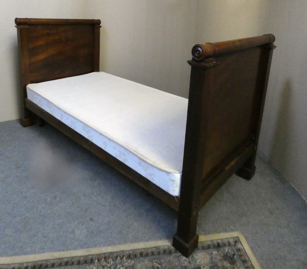 An antique dark mahogany single bed frame featuring a rolled scroll cresting rail on the headboard and footboard.