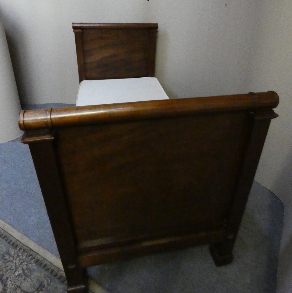 An antique dark mahogany single bed frame featuring a rolled scroll cresting rail on the headboard and footboard. View III