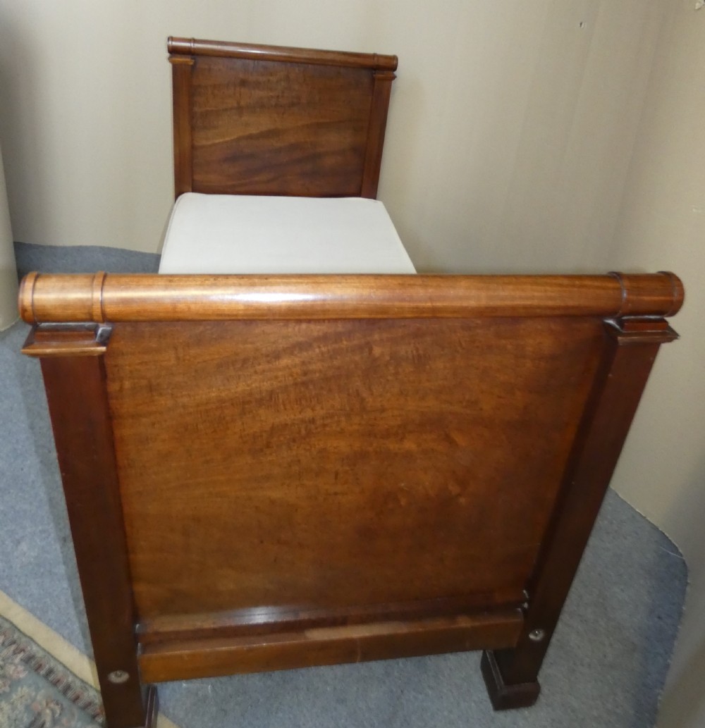 An antique dark mahogany single bed frame featuring a rolled scroll cresting rail on the headboard and footboard. View V