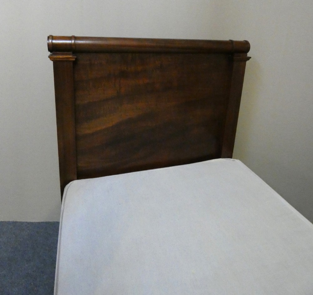 An antique dark mahogany single bed frame featuring a rolled scroll cresting rail on the headboard and footboard. View VI