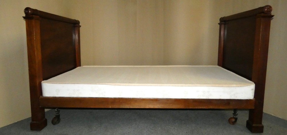 An antique dark mahogany single bed frame featuring a rolled scroll cresting rail on the headboard and footboard. View IX