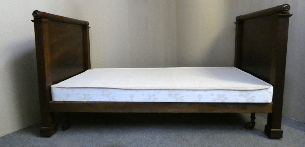 An antique dark mahogany single bed frame featuring a rolled scroll cresting rail on the headboard and footboard. View X
