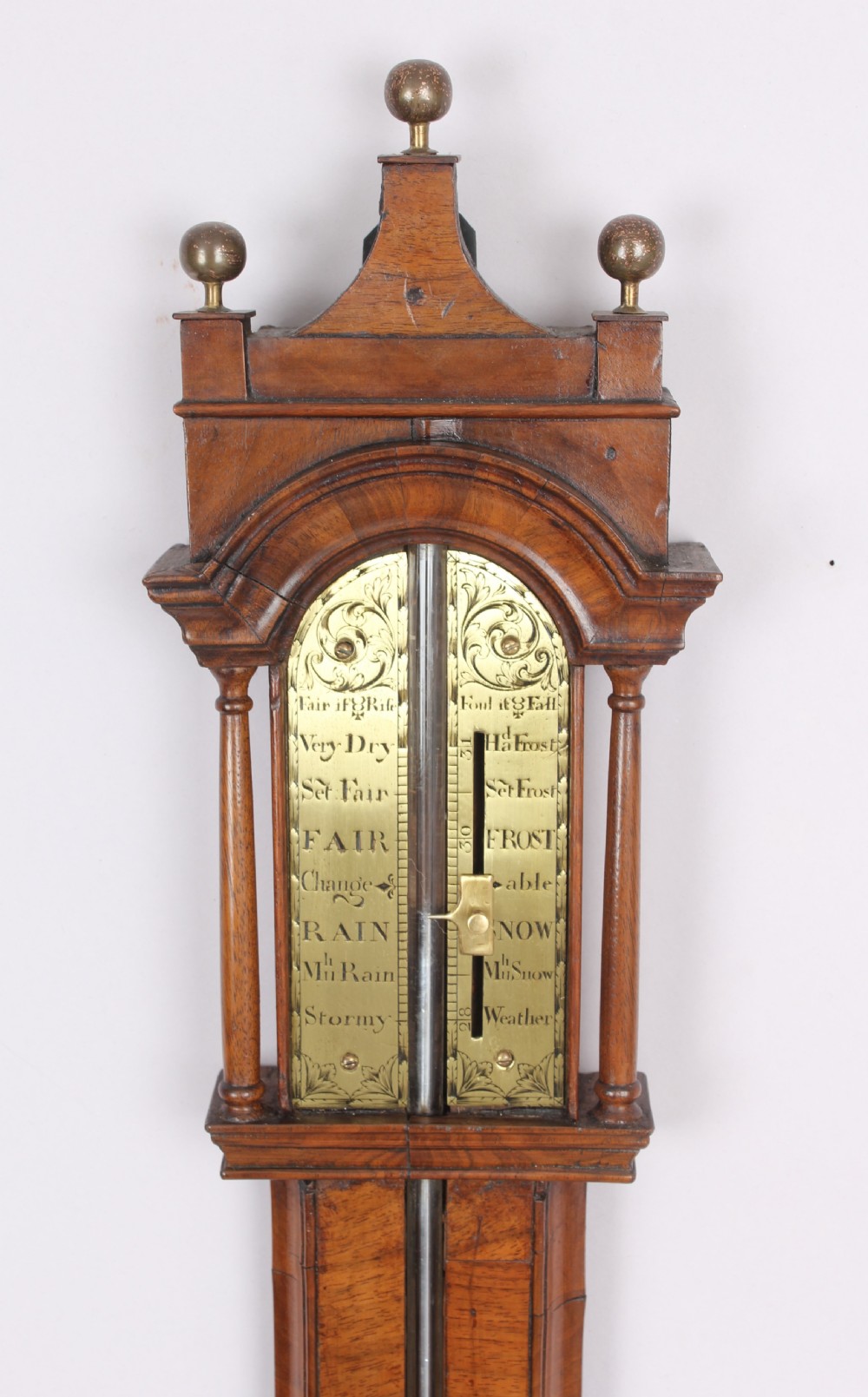 An early 18th-century walnut stick barometer featuring an arched brass register plate, turned side pillars, brass finials, and a turned hemispherical cistern cover. View II