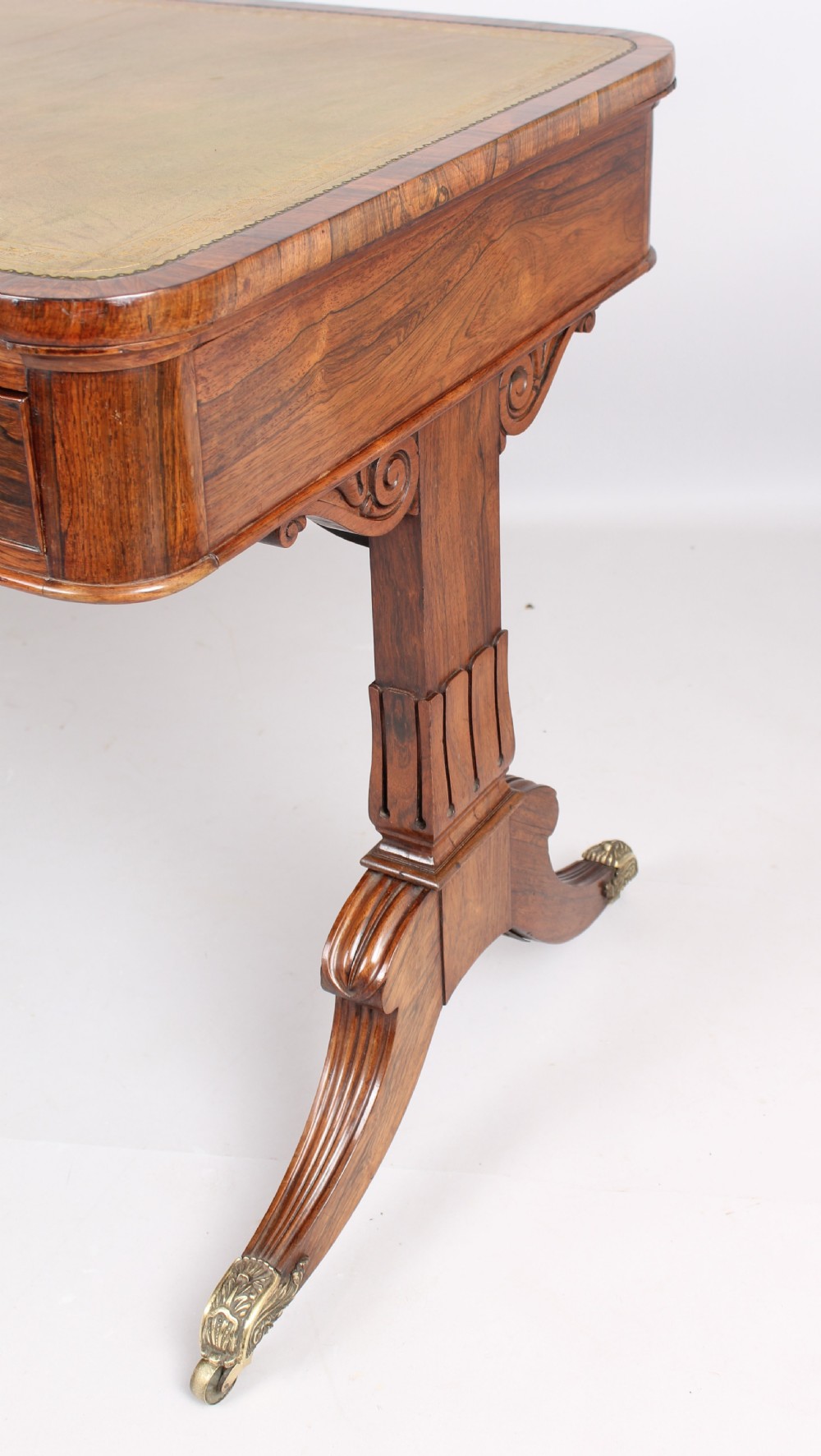 An antique rosewood writing table featuring a green leather inset surface, dual frieze drawers with wooden knobs, and splayed legs with brass paw castors. View II