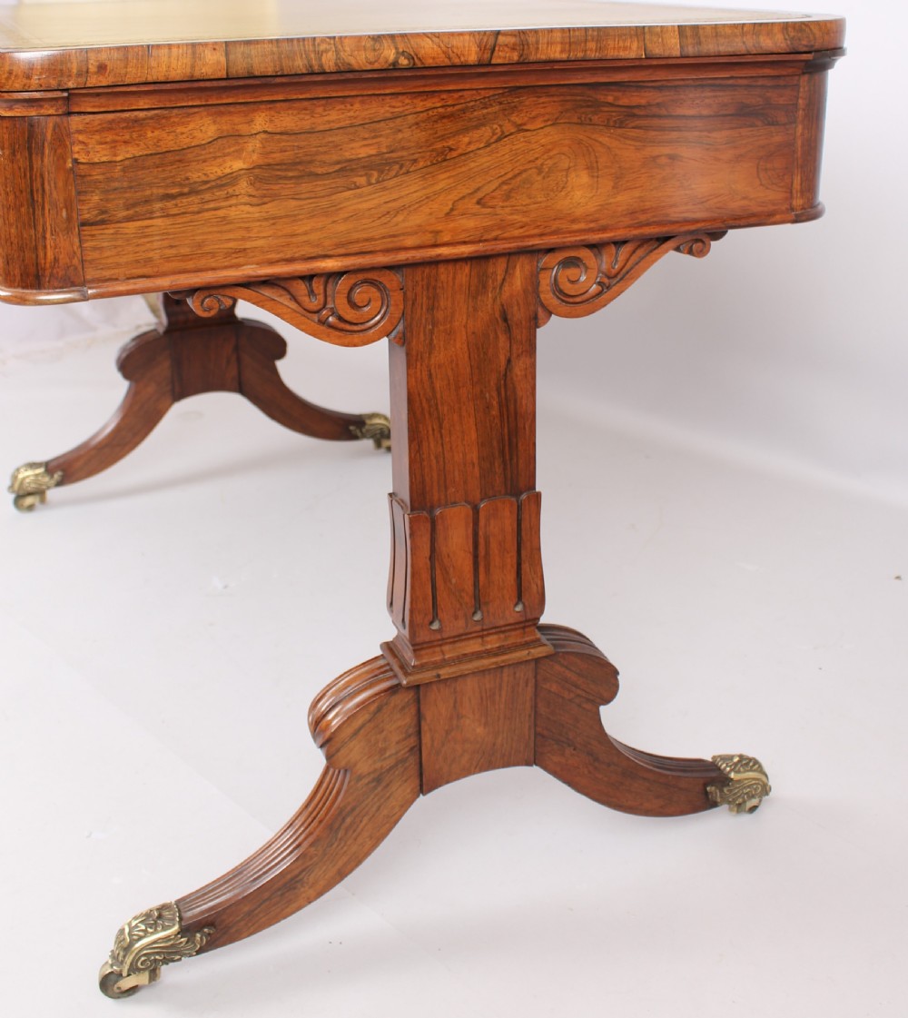An antique rosewood writing table featuring a green leather inset surface, dual frieze drawers with wooden knobs, and splayed legs with brass paw castors. View III