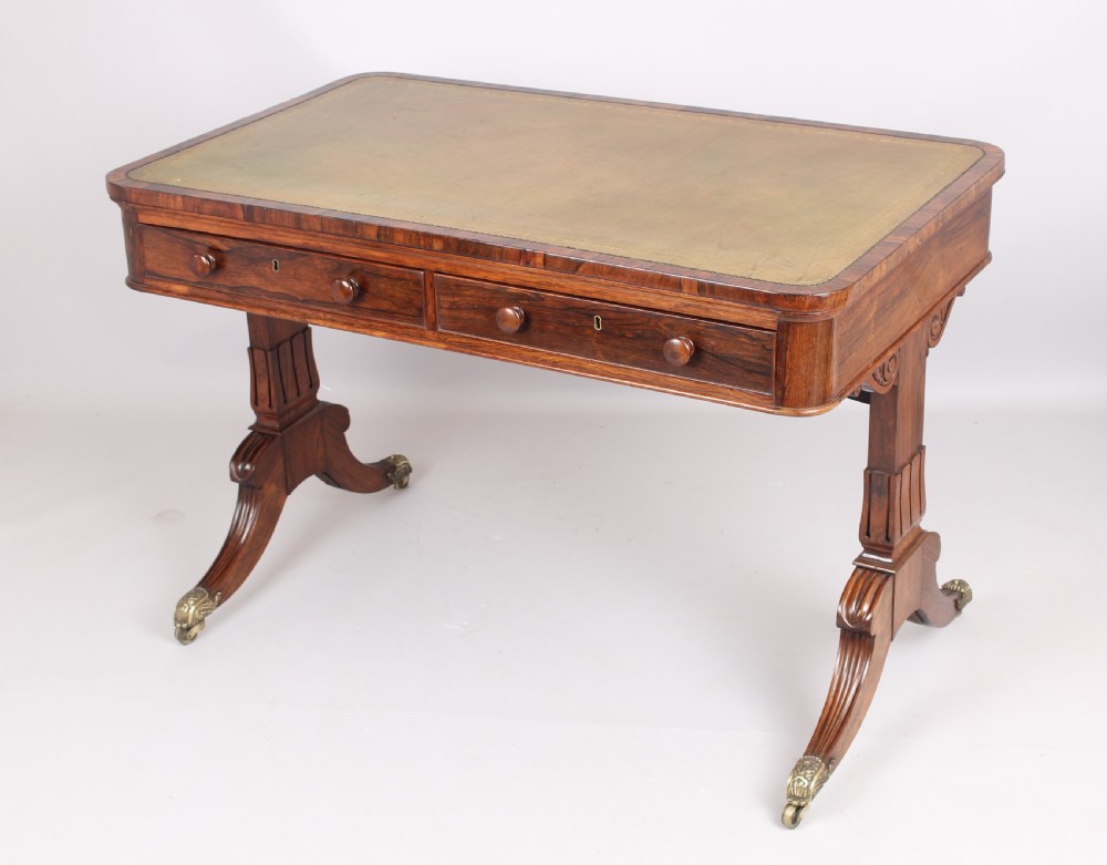 An antique rosewood writing table featuring a green leather inset surface, dual frieze drawers with wooden knobs, and splayed legs with brass paw castors. View V