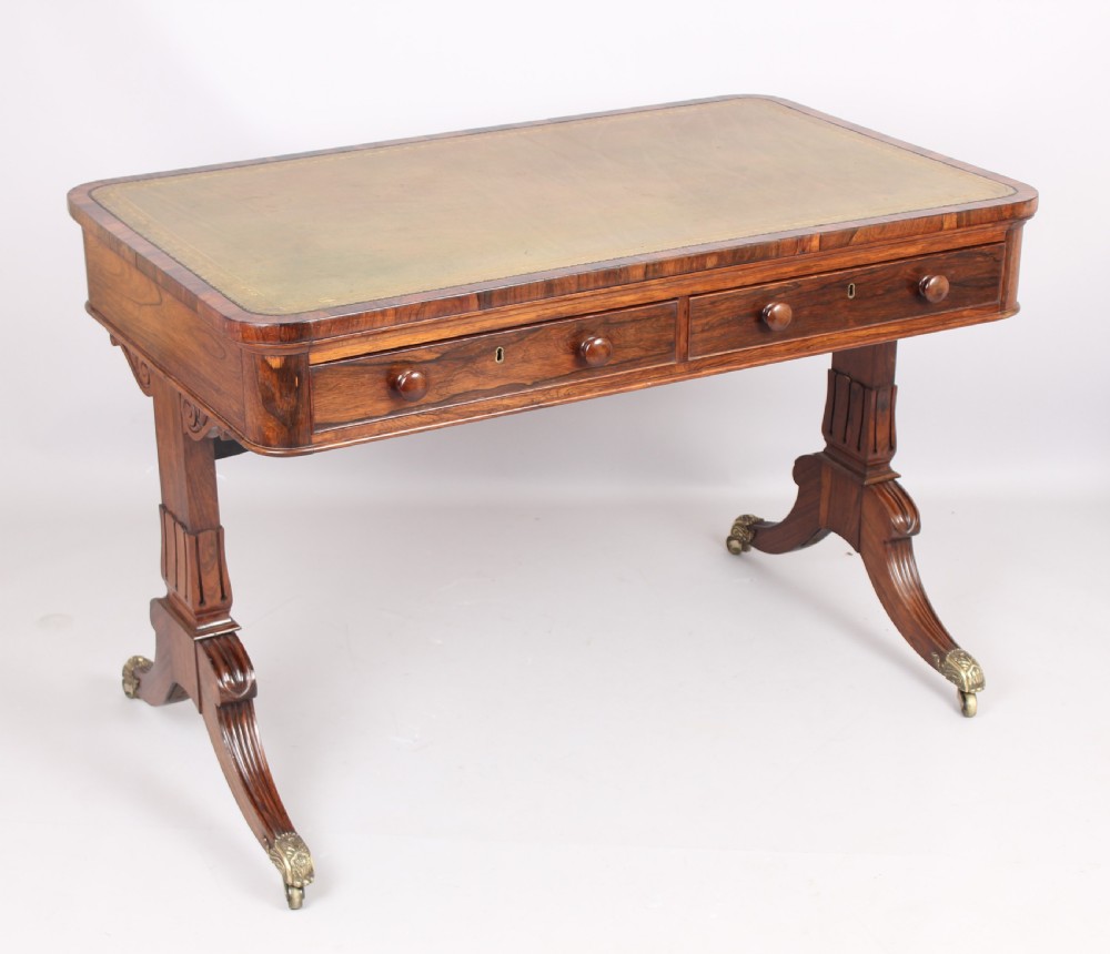 An antique rosewood writing table featuring a green leather inset surface, dual frieze drawers with wooden knobs, and splayed legs with brass paw castors. View VI