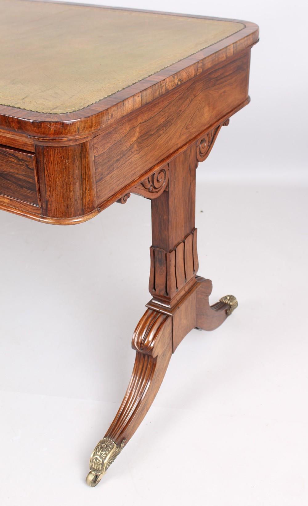 An antique rosewood writing table featuring a green leather inset surface, dual frieze drawers with wooden knobs, and splayed legs with brass paw castors. View VII