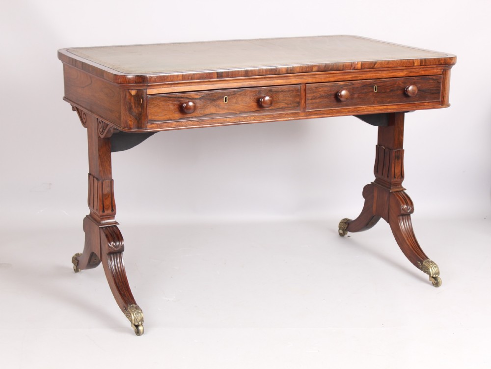 An antique rosewood writing table featuring a green leather inset surface, dual frieze drawers with wooden knobs, and splayed legs with brass paw castors. View VIII
