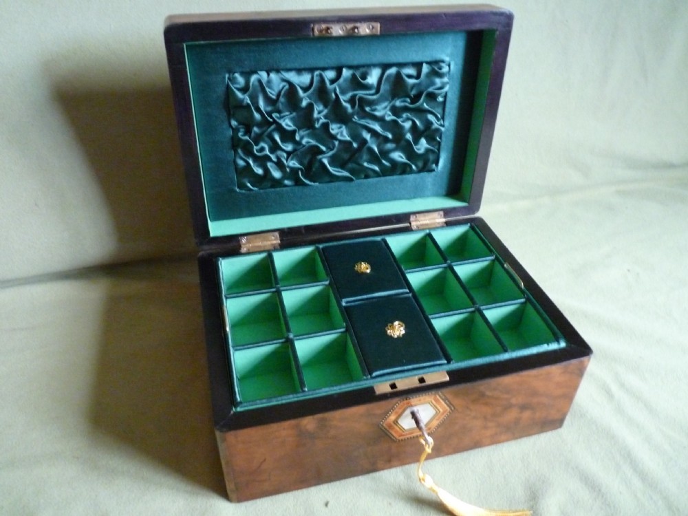An open Victorian burr walnut jewellery box with a green silk lining, partitioned tray, and mother-of-pearl escutcheon.