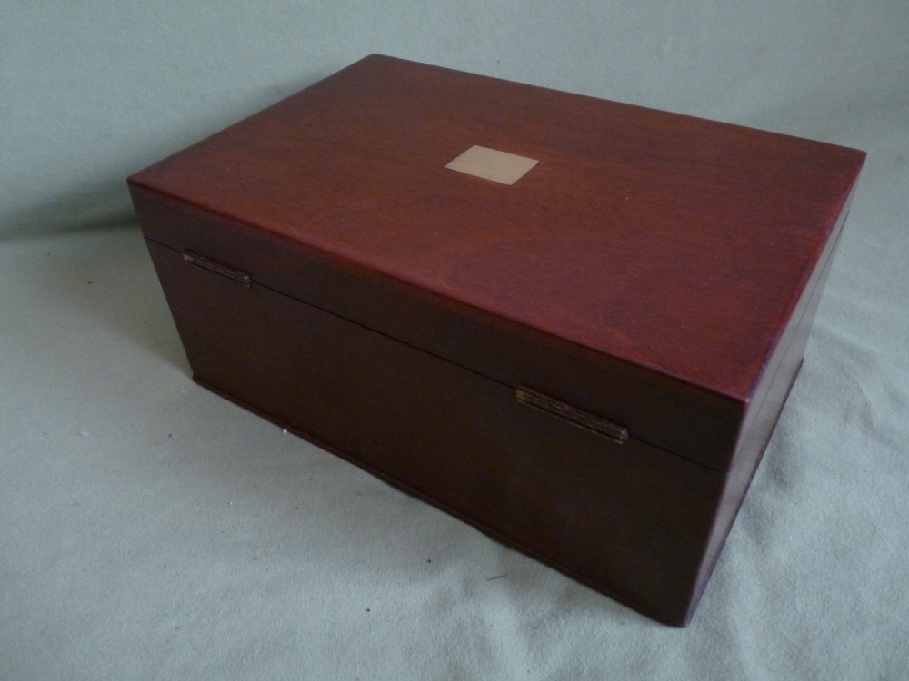 An open mahogany jewellery box featuring a pink-lined interior with tiered compartments, a lower drawer, and brass fittings. View VI