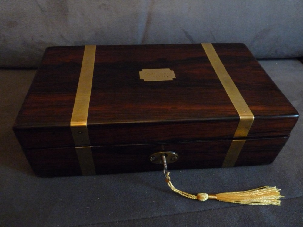 A dark rosewood rectangular box featuring polished brass straps across the lid and front with a central brass plaque and keyhole.