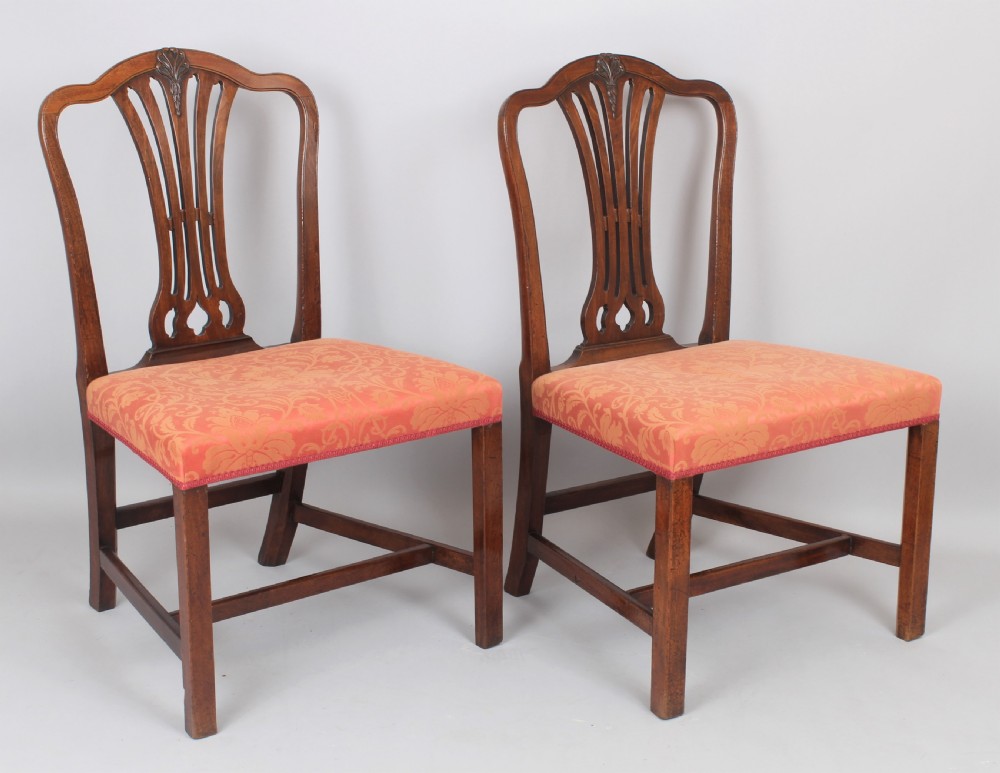 A pair of George III period mahogany side chairs featuring pierced back splats and seats upholstered in coral patterned damask.