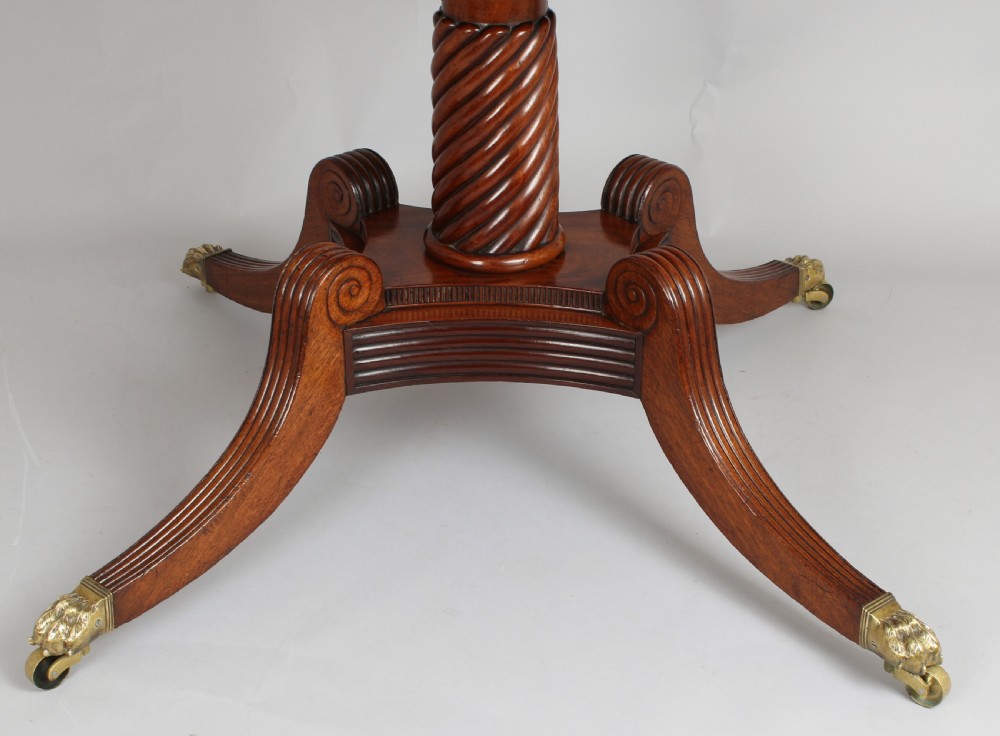 A George IV mahogany breakfast table featuring a polished rectangular top with rounded corners, supported by a spiral-carved pedestal and four reeded legs with brass lion paw castors. View II