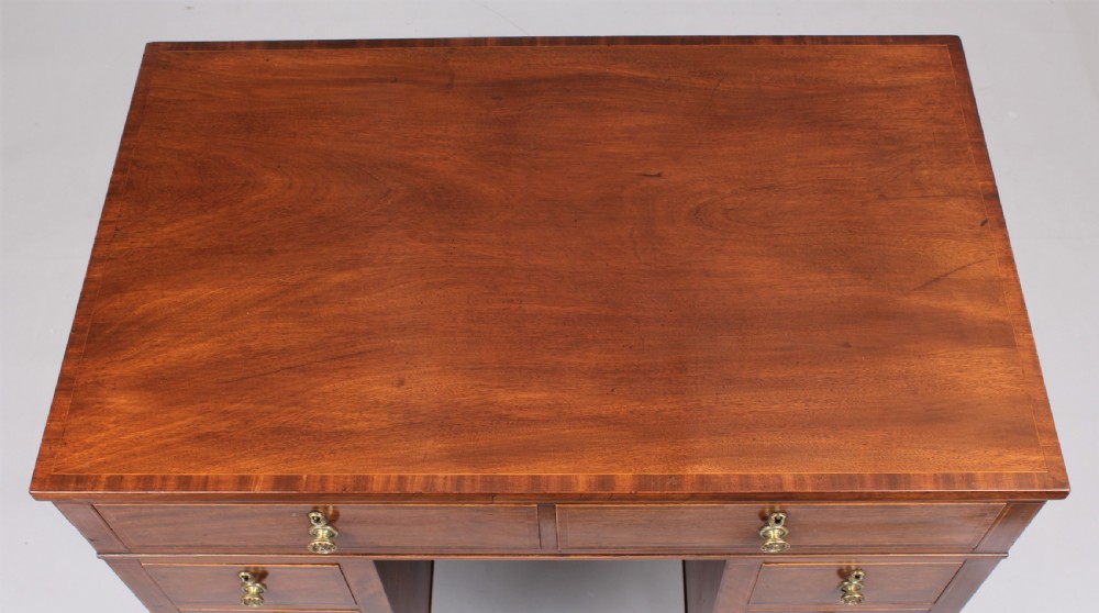 A late 18th-century Sheraton period mahogany kneehole desk featuring multiple drawers with brass handles, inlaid boxwood stringing, and square tapered legs on castors. View V