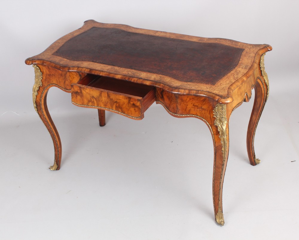 A French Rococo style burr walnut writing table featuring cabriole legs, ornate brass mounts, and a dark brown leather writing top. View II