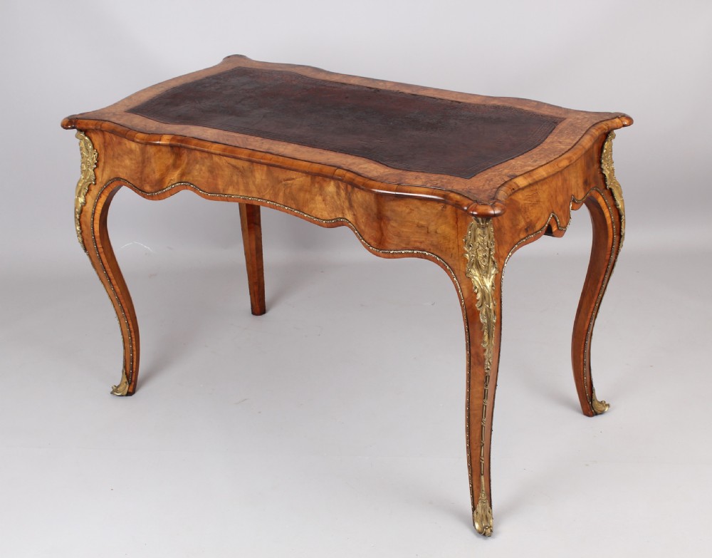 A French Rococo style burr walnut writing table featuring cabriole legs, ornate brass mounts, and a dark brown leather writing top. View V