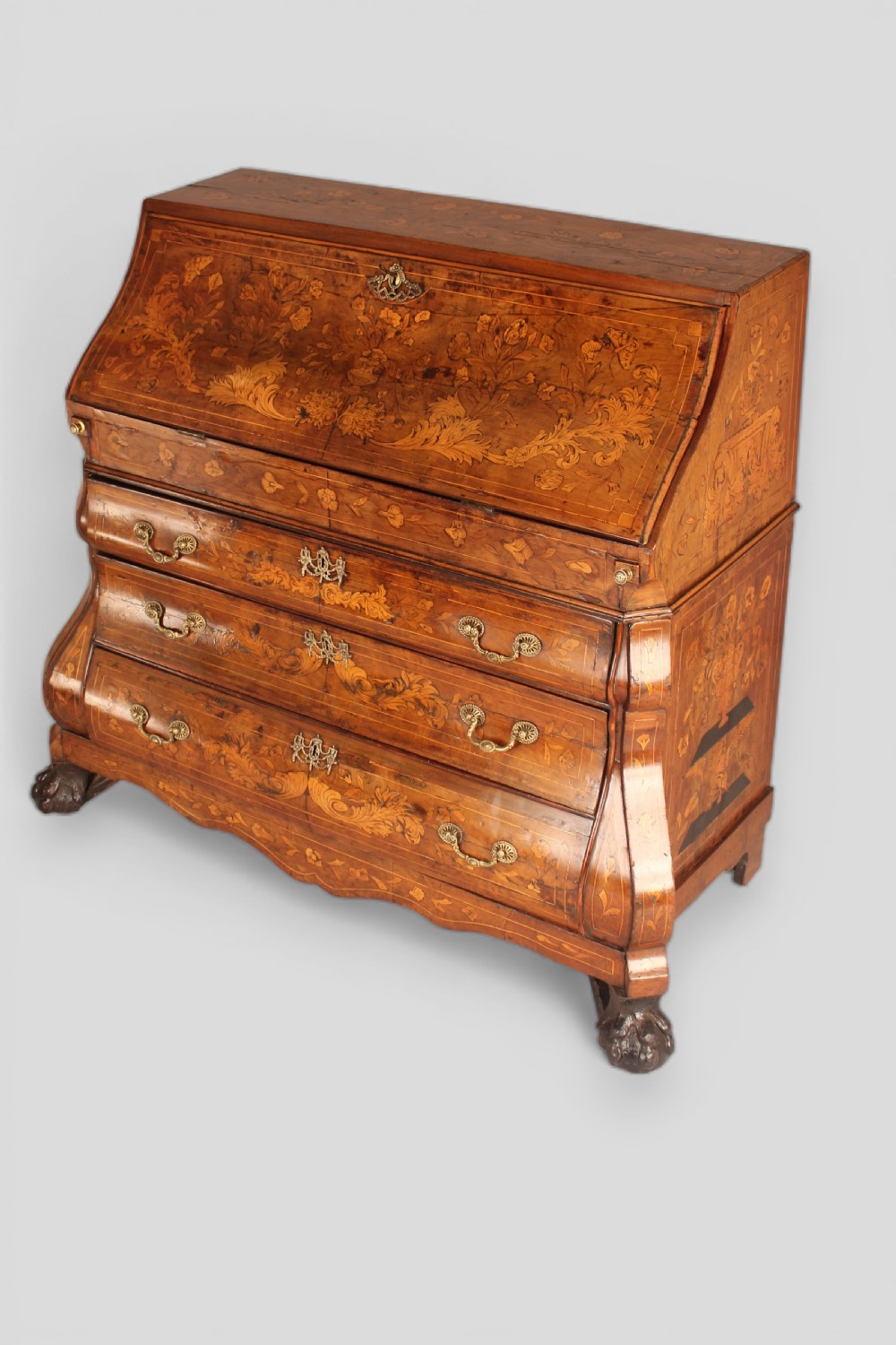 An 18th-century walnut slant-front bureau featuring intricate floral marquetry, three curved bombe drawers, brass drop handles, and carved feet.