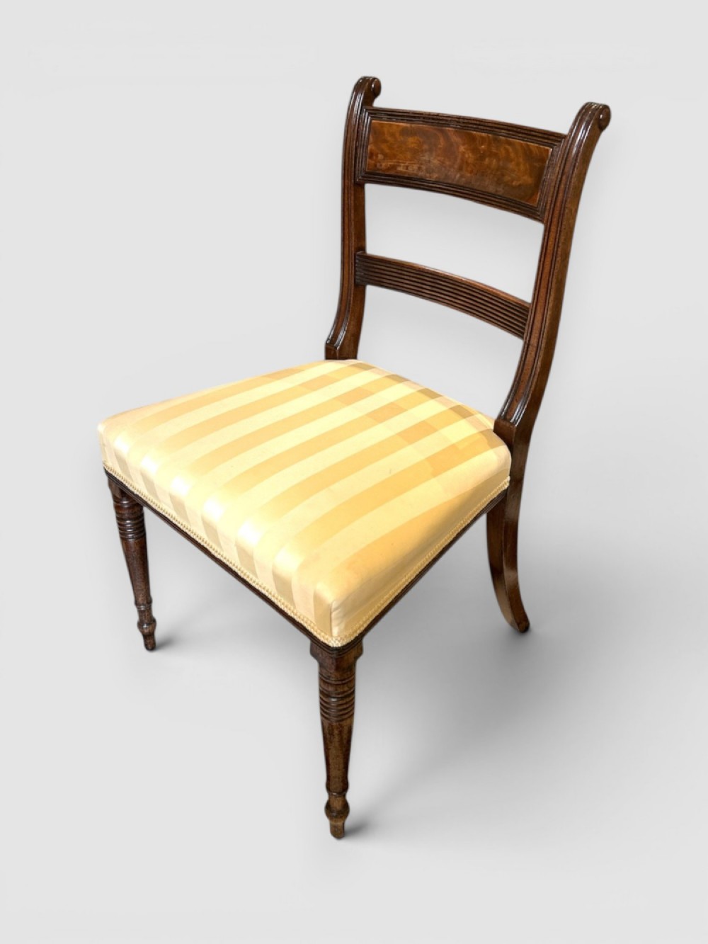 An antique Regency mahogany dining chair featuring turned front legs, sabre back legs, and a yellow striped upholstered seat. View II