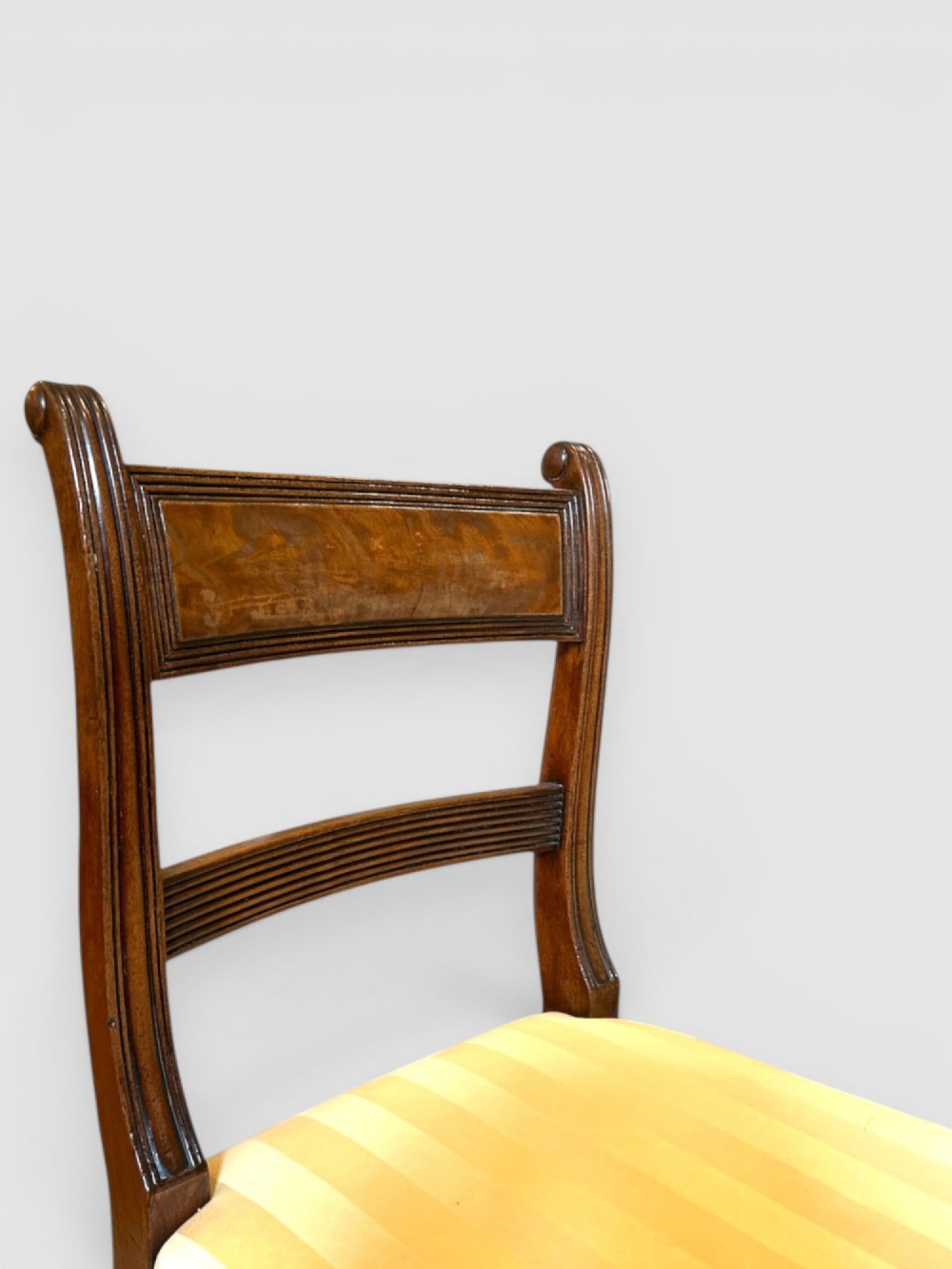 An antique Regency mahogany dining chair featuring turned front legs, sabre back legs, and a yellow striped upholstered seat. View III
