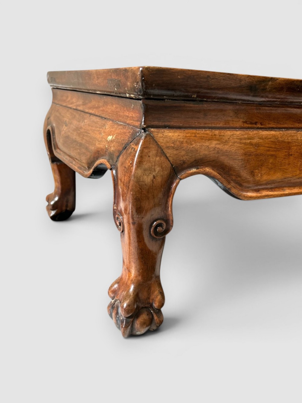 A low rectangular warm brown wooden Chinese opium table featuring short cabriole legs, carved scrolled feet, and a polished panel top. View II