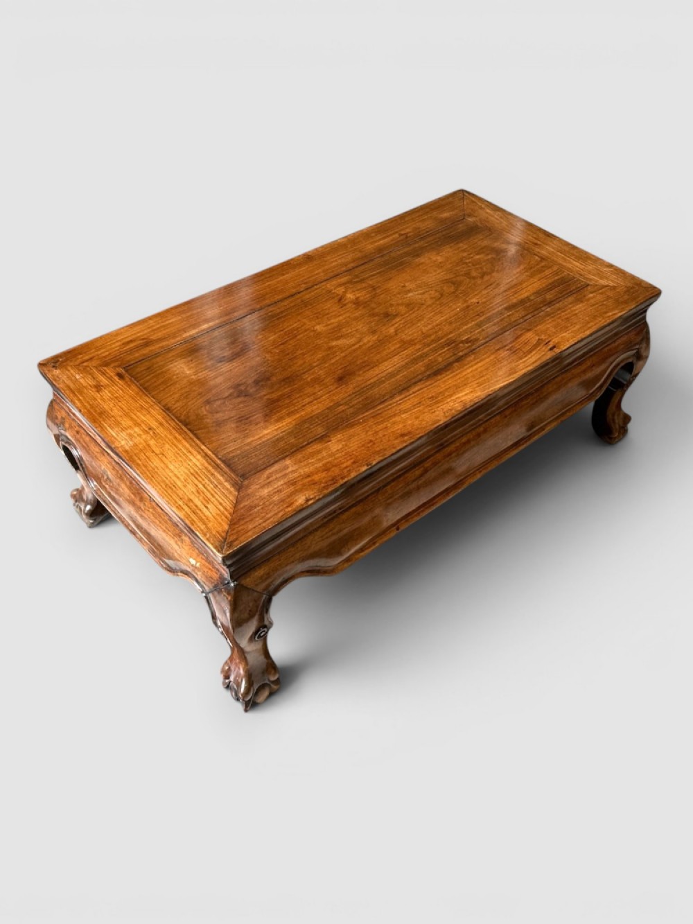 A low rectangular warm brown wooden Chinese opium table featuring short cabriole legs, carved scrolled feet, and a polished panel top. View III