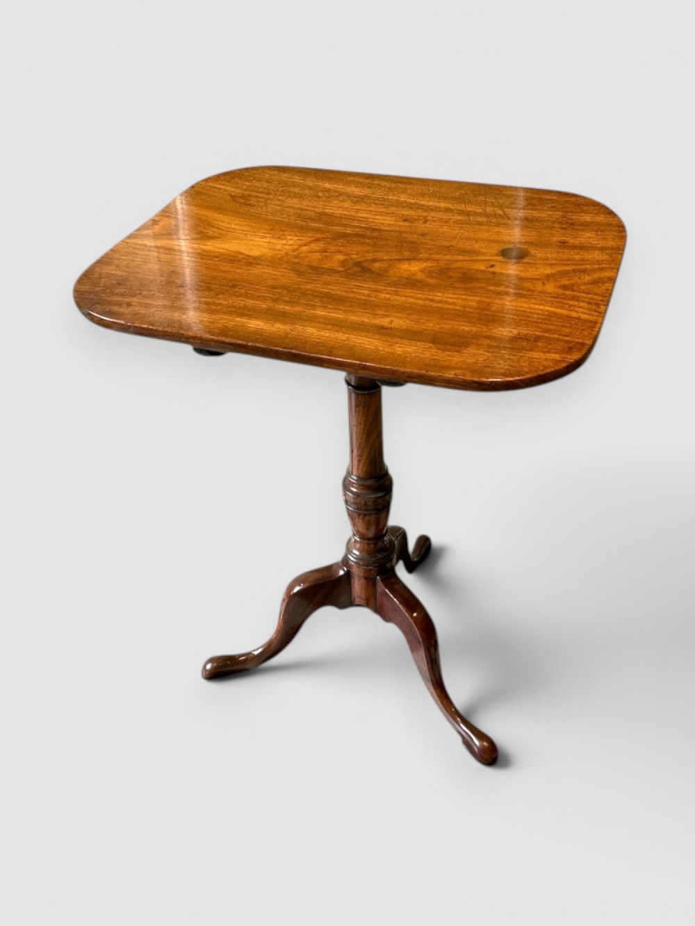 An antique dark mahogany tilt-top table featuring a rectangular surface with rounded corners supported by a turned central column and three curved legs.