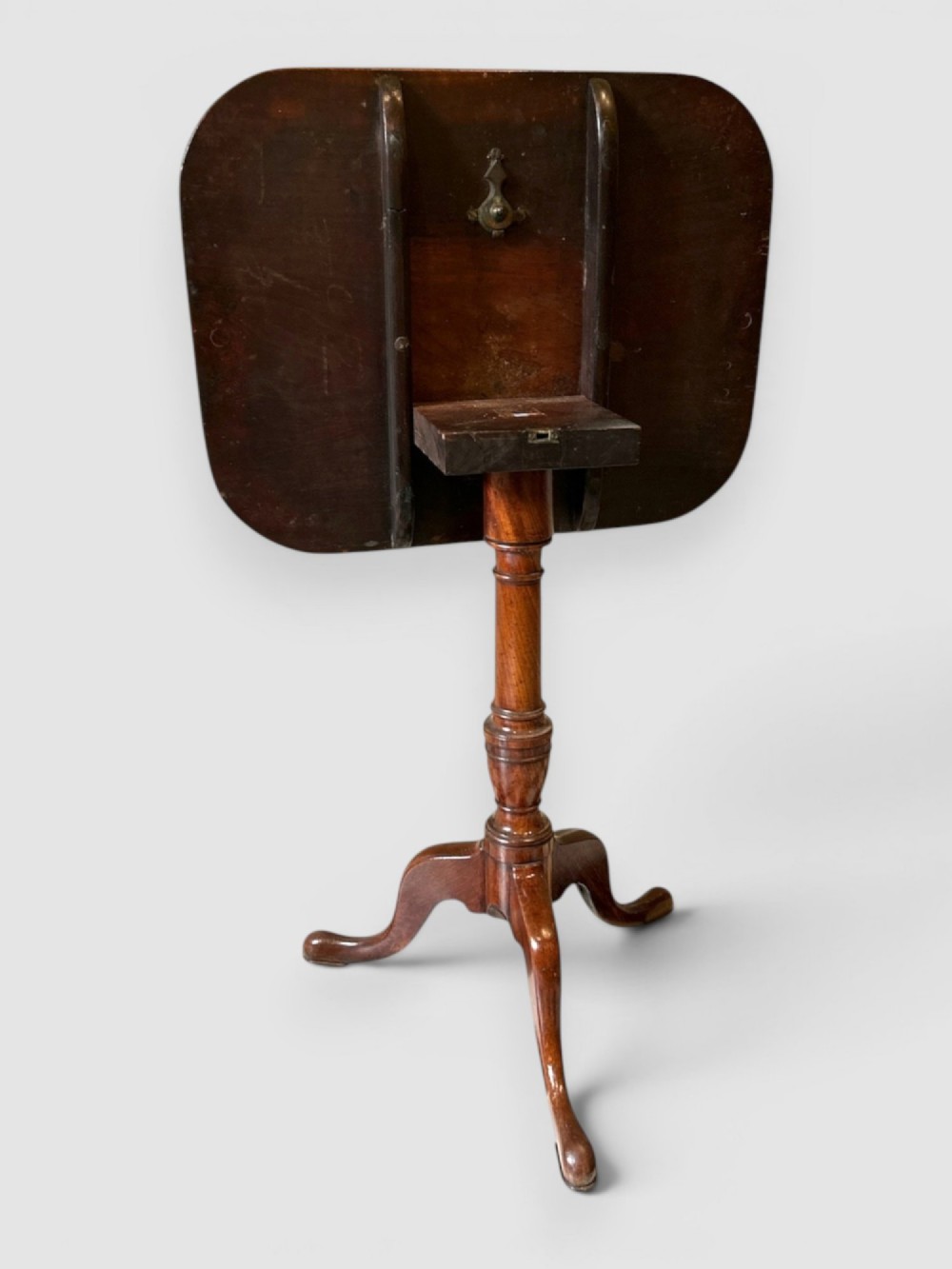 An antique dark mahogany tilt-top table featuring a rectangular surface with rounded corners supported by a turned central column and three curved legs. View II