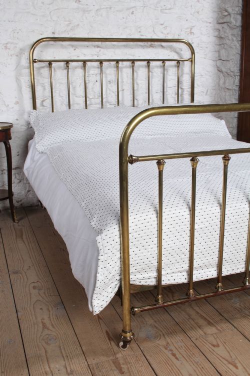 fig 1. An antique French all-brass double bed frame featuring a rounded headboard and footboard with slender vertical spindles set on castor wheels.