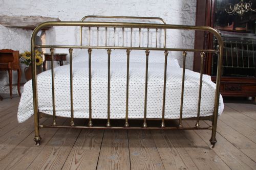 fig 2. An antique French all-brass double bed frame featuring a rounded headboard and footboard with slender vertical spindles set on castor wheels.