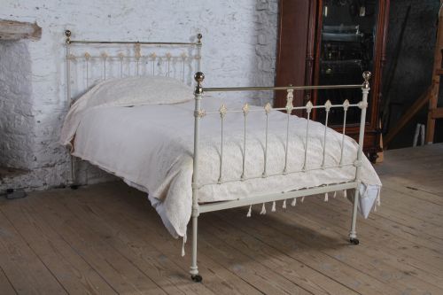 fig 1. A Victorian cream-painted iron and brass three-quarter bedstead featuring vertical spindles, decorative cast motifs, and polished brass top rails with spherical finials.