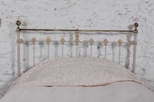 fig 2. A Victorian cream-painted iron and brass three-quarter bedstead featuring vertical spindles, decorative cast motifs, and polished brass top rails with spherical finials.