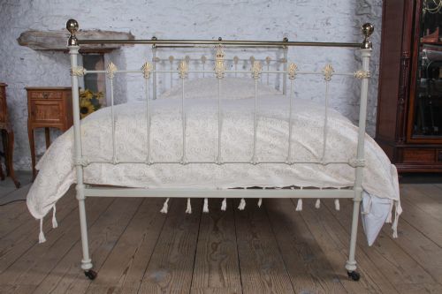 fig 3. A Victorian cream-painted iron and brass three-quarter bedstead featuring vertical spindles, decorative cast motifs, and polished brass top rails with spherical finials.
