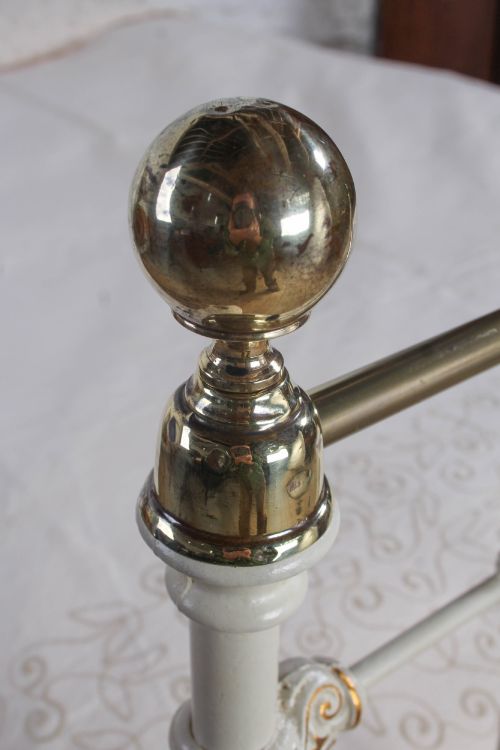 fig 4. A Victorian cream-painted iron and brass three-quarter bedstead featuring vertical spindles, decorative cast motifs, and polished brass top rails with spherical finials.